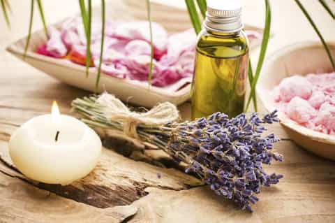 Spa essentials with lavender bundle, candle, essential oil, and pink flowers on wood