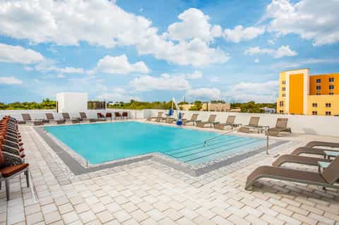 Rooftop pool with bright turquoise water, lounge chairs, modern yellow building, and expansive sky view