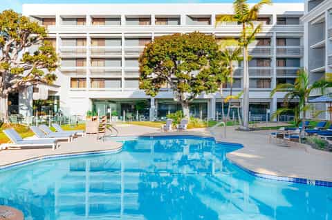Modern hotel courtyard with blue pool, lounge chairs, and white residential building