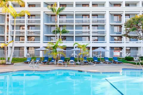 Resort pool with clear turquoise water, blue loungers, palm trees, and apartment building