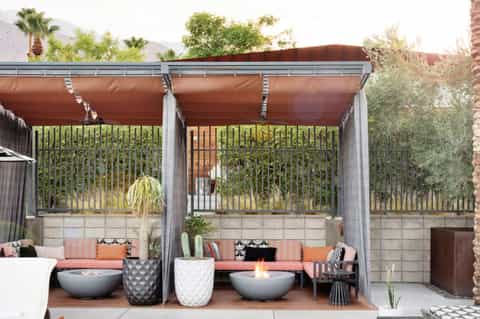 Modern desert patio with retractable shade canopies, fire bowls, coral cushions, and mountain backdrop