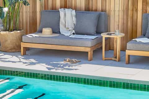 Modern wooden seating area with gray cushions and side table overlooking lap pool with green tile border