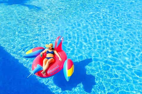 Woman on colorful inflatable pool float in crystal clear blue swimming pool water