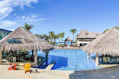 Tropical resort pool area with thatched-roof cabanas and palm trees