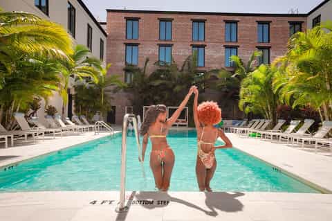 Two women in pool within tropical courtyard surrounded by palm trees and brick building