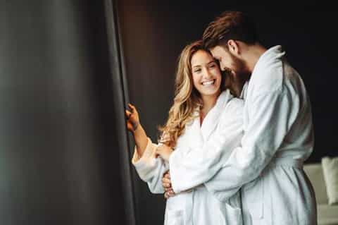 Couple in spa robes embracing near window in intimate resort spa setting