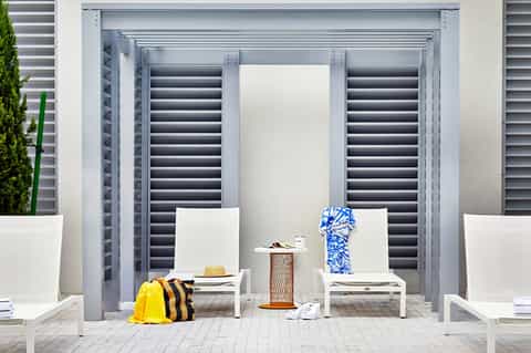 Modern poolside cabana with white lounge chairs and dark shuttered doors