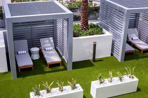 Modern resort lounge area with white slatted cabanas, wooden loungers, and manicured lawn