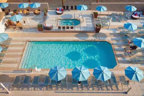 Resort pool deck with blue umbrellas, lounge chairs, and multi-level hot tubs from above