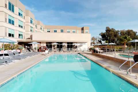 Hotel pool deck with turquoise water, white umbrellas, lounge chairs, and modern building facade