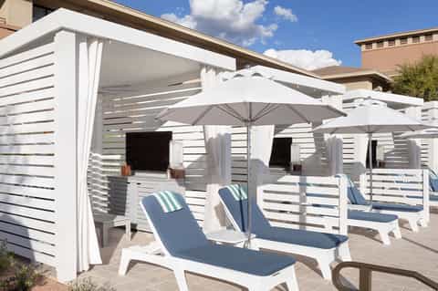 Outdoor cabanas with white pergolas, blue lounge chairs, umbrellas, and striped privacy screens