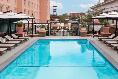 Rooftop swimming pool with loungers and black umbrellas surrounded by historic brick buildings