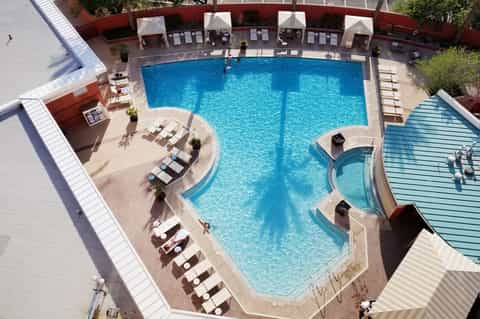 Overhead view of curved resort pool with cabanas, lounge chairs, and spa facilities surrounded by building