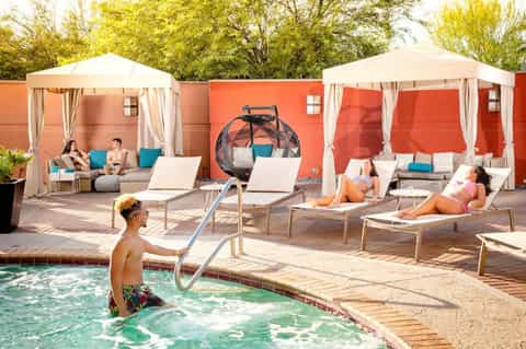 Resort pool deck with loungers, shade structures, and guests relaxing under umbrellas