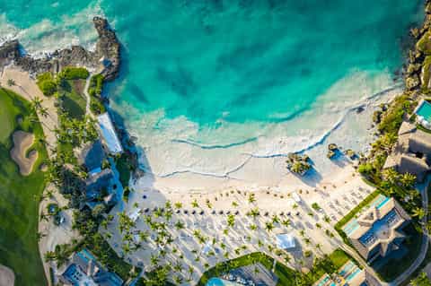 Aerial view of beachfront resort with turquoise ocean, white sand, palm trees, and multiple swimming pools