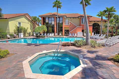 Resort pool and hot tub area with colorful buildings, lounge chairs, and palm trees