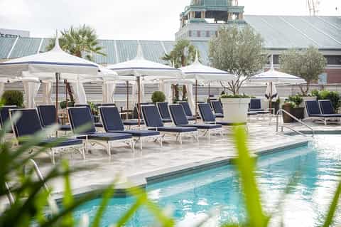 Luxury poolside lounge with white cabana tents, blue loungers, and historic architecture