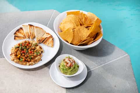 Poolside appetizers: hummus with pita, tortilla chips, guacamole dip, and turquoise pool