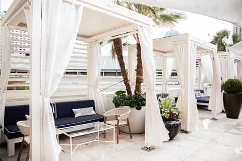 White cabana lounge area with flowing curtains, palm trees, and ocean views