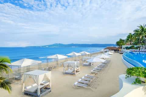 Beachfront resort with white cabanas, lounge chairs, turquoise pool, and ocean view