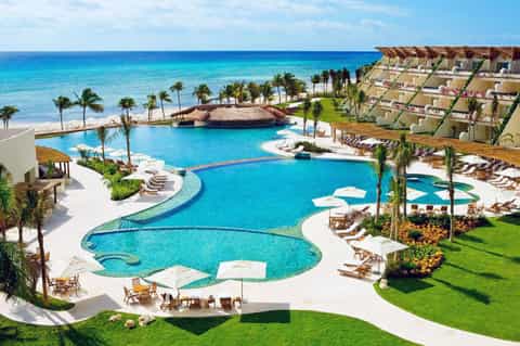 Aerial view of large resort complex with curved pool, beach, and tiered accommodations