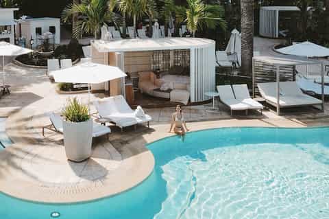 Resort pool area with cabanas, loungers, umbrellas, and tropical landscaping