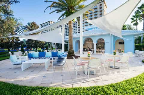 Coastal resort patio with blue and white seating, sail shade canopy, and beach access