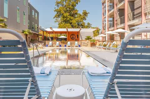 Modern resort pool with lounge chairs, peace sign wall decoration, and contemporary apartment buildings