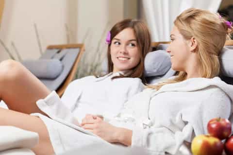 Two women in white robes relaxing in spa treatment room with modern furnishings