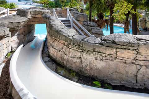 Water slide carved through natural stone formations with turquoise pools and palm trees