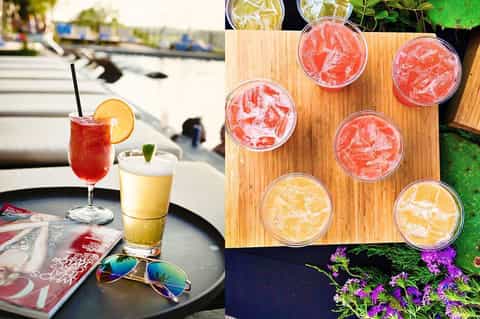 Colorful cocktails and beverages displayed on wooden board beside waterfront seating area with orange loungers