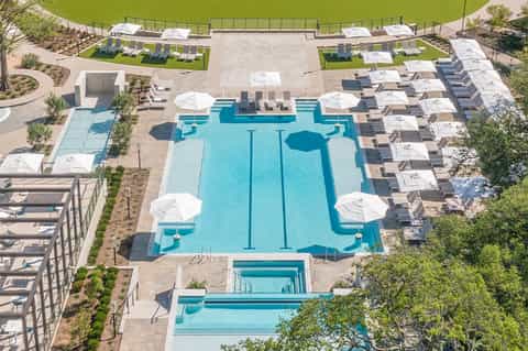 Aerial view of large resort swimming pool complex with lounge chairs and white umbrellas