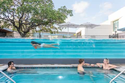 Swimmer doing freestyle strokes in lap pool with hot tub and umbrellas nearby