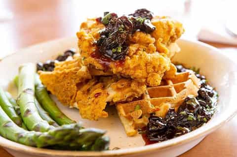Gourmet fried chicken and waffles with greens served on white plate in upscale dining
