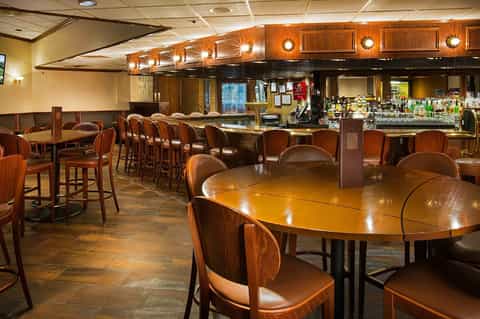 Classic hotel bar lounge with wooden furniture, bar counter with bottles, and warm ambient lighting