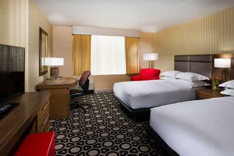 Hotel room with two queen beds, wood furnishings, patterned carpet, and warm ambient lighting