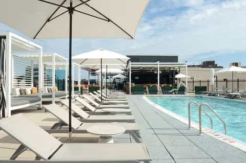 Rooftop pool deck with white umbrellas, lounge chairs, and city skyline views