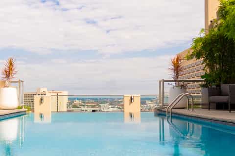 Rooftop infinity pool overlooking city skyline with palm trees and modern hotel architecture