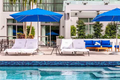 Modern pool deck with white loungers, blue umbrellas, and contemporary hotel building