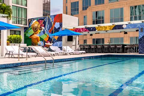 Modern resort pool with colorful mural backdrop, blue umbrellas, and lounge chairs