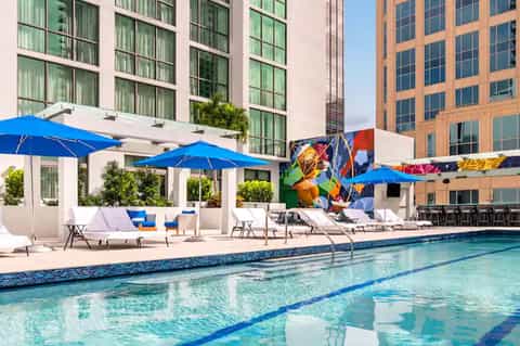 Resort pool with blue umbrellas, loungers, colorful mural art, and modern building backdrop