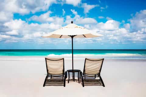 Two loungers with umbrella and small table on pristine white sand beach facing turquoise ocean and sky