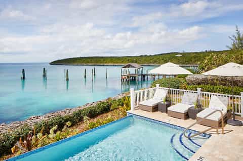 Oceanfront infinity pool overlooking turquoise water, dock, and tropical vegetation