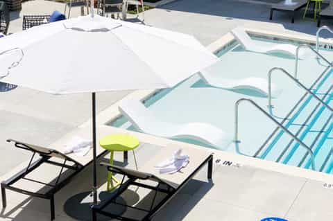 Resort pool deck with white umbrella, lounge chairs, and spa pools