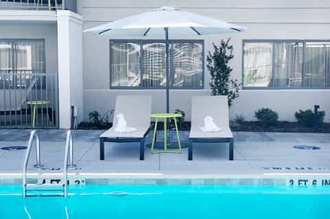 Modern poolside lounge with white loungers, umbrella, and spa building