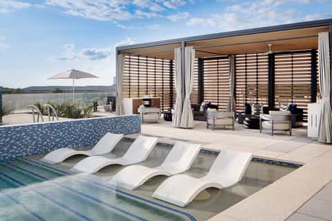 Modern resort pool with sunbed loungers, blue tile accent, covered cabana structure, and mountain views