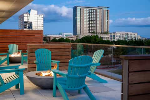 Turquoise Adirondack chairs around fire pit on rooftop with city skyline