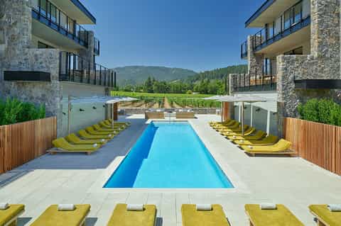 Resort infinity pool with yellow loungers flanked by stone buildings and mountain forest views