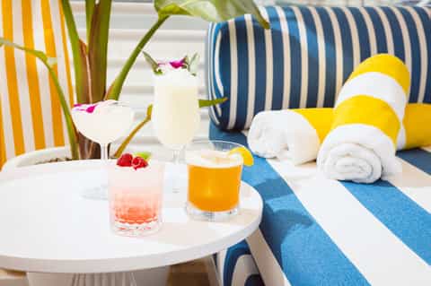 Colorful poolside drinks with striped beach chairs, towels, and tropical flowers on small table