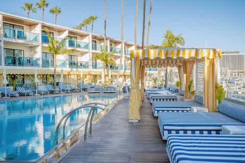 Modern resort pool deck with yellow striped cabanas, lounge chairs, and high-rise building